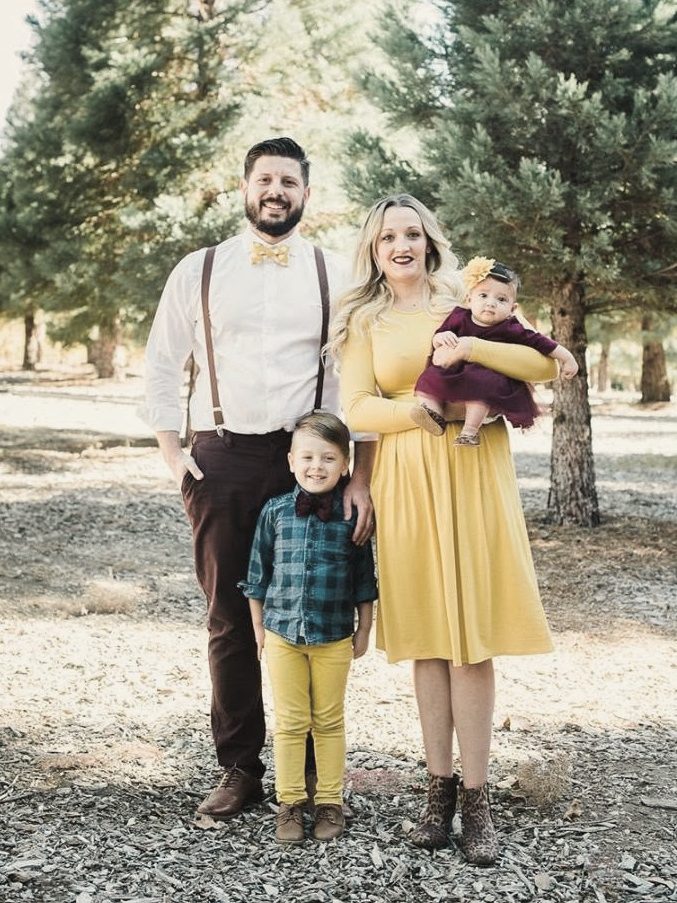 Family of four in a pine grove, mom in a yellow dress
