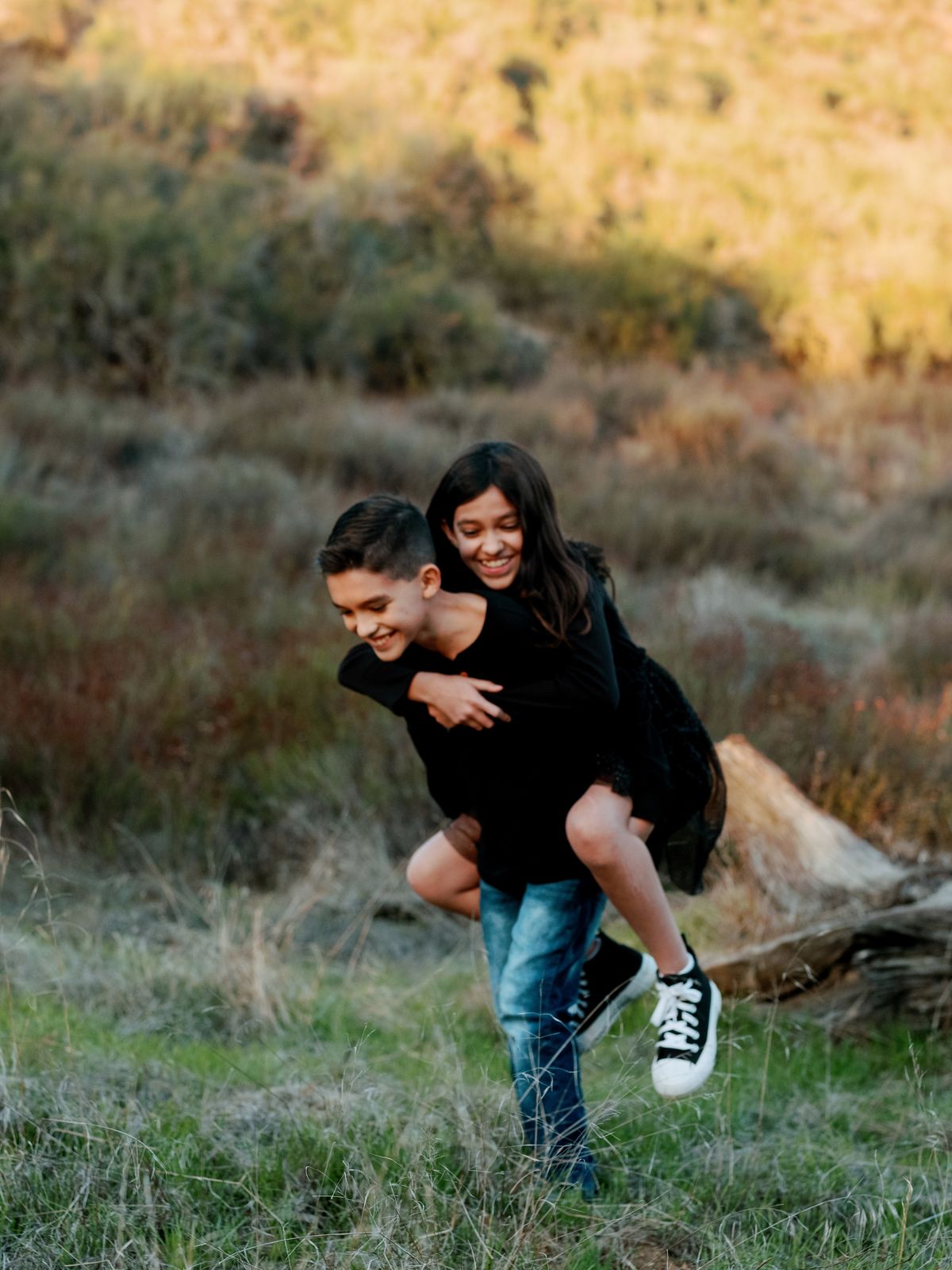 A boy giving his sister a piggyback ride in tall grass