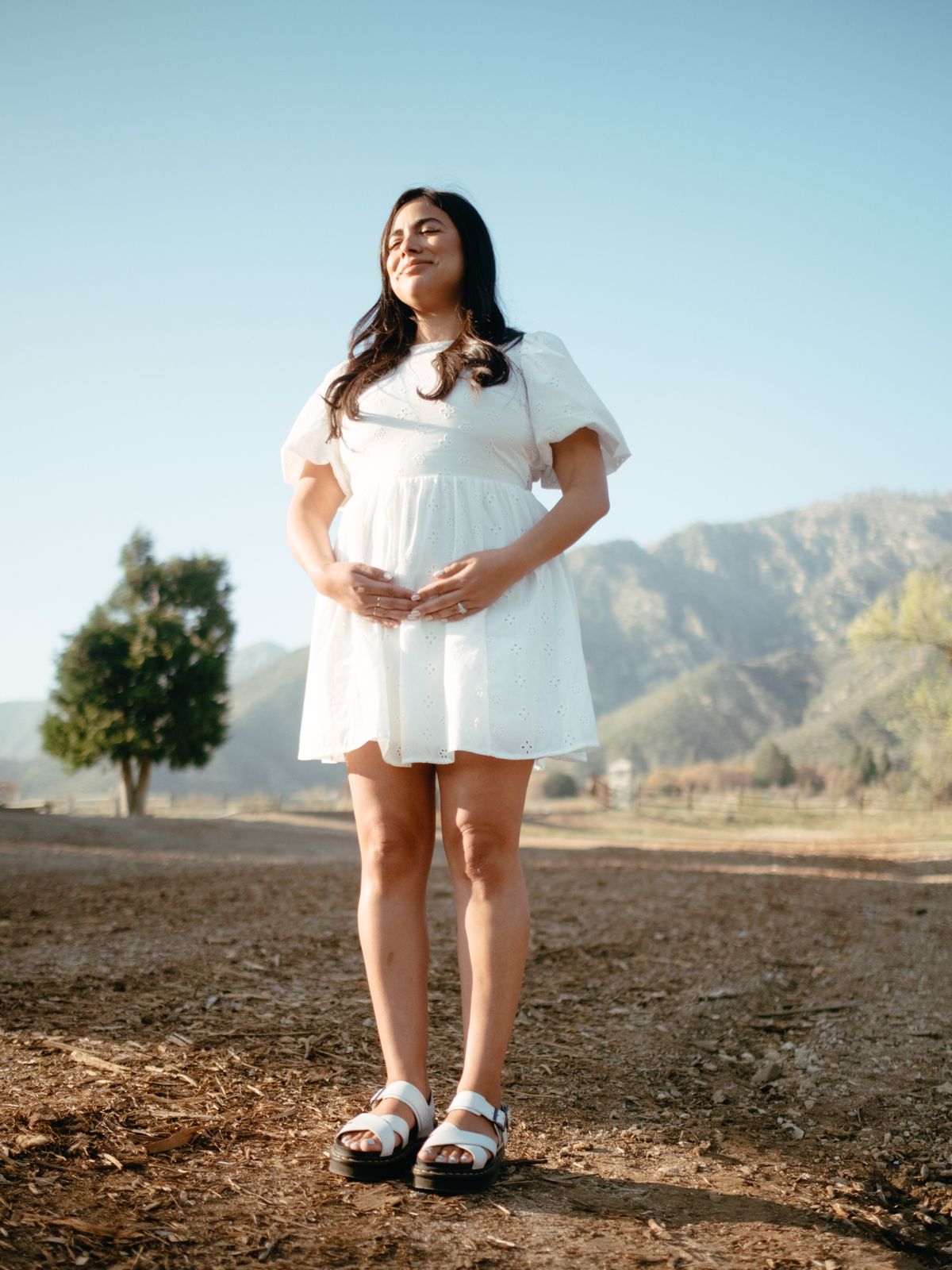 An expecting mother in a white dress standing in an open field
