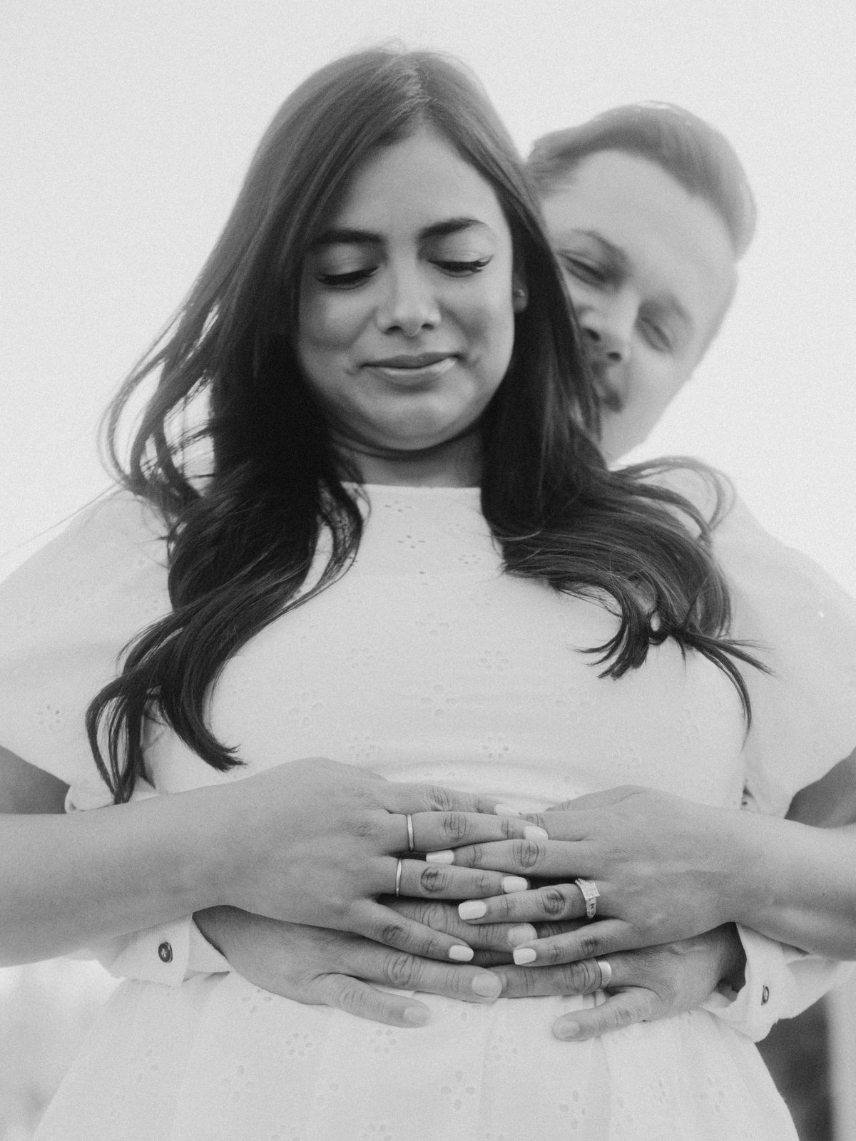 Black and white photo of a couple's hands over her pregnant belly