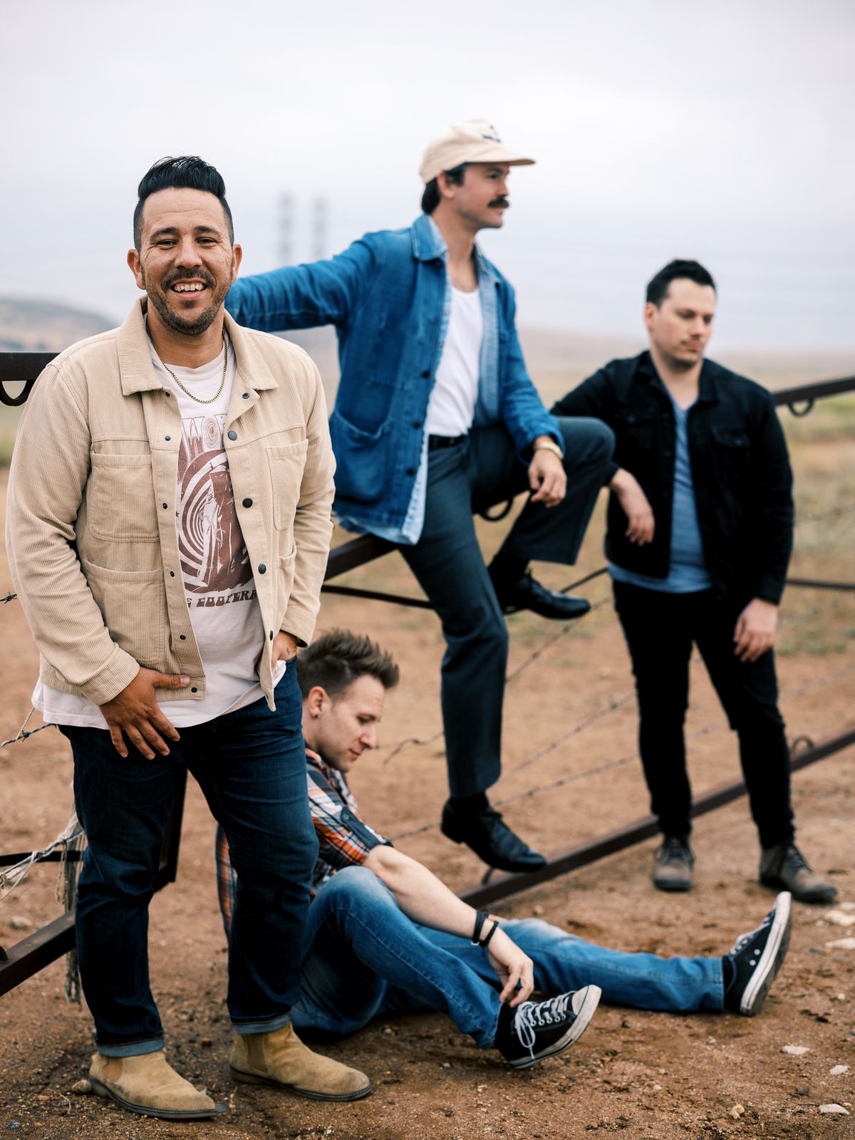 A four-piece band posing at a ranch gate