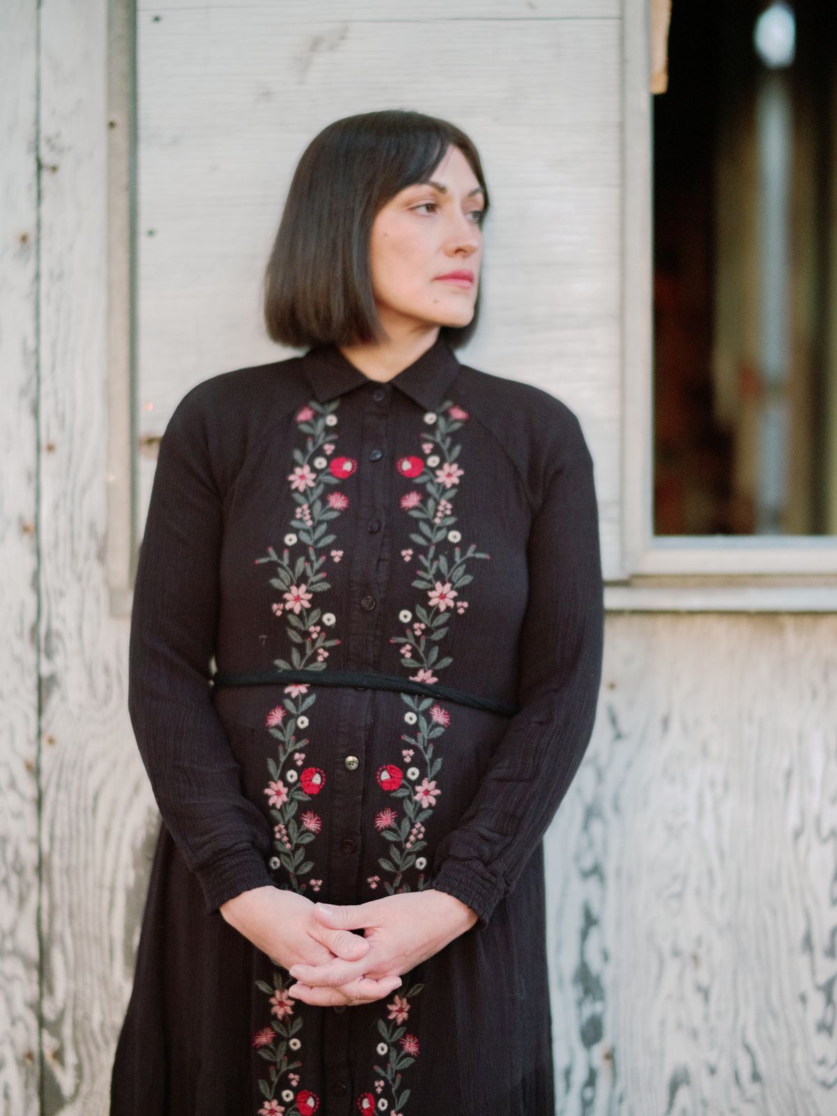 A woman in an embroidered dress standing by a weathered white shed