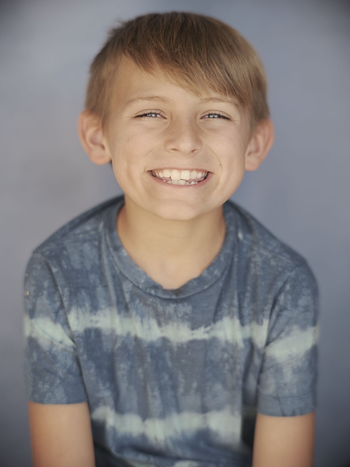 A boy grinning in front of a painted blue backdrop